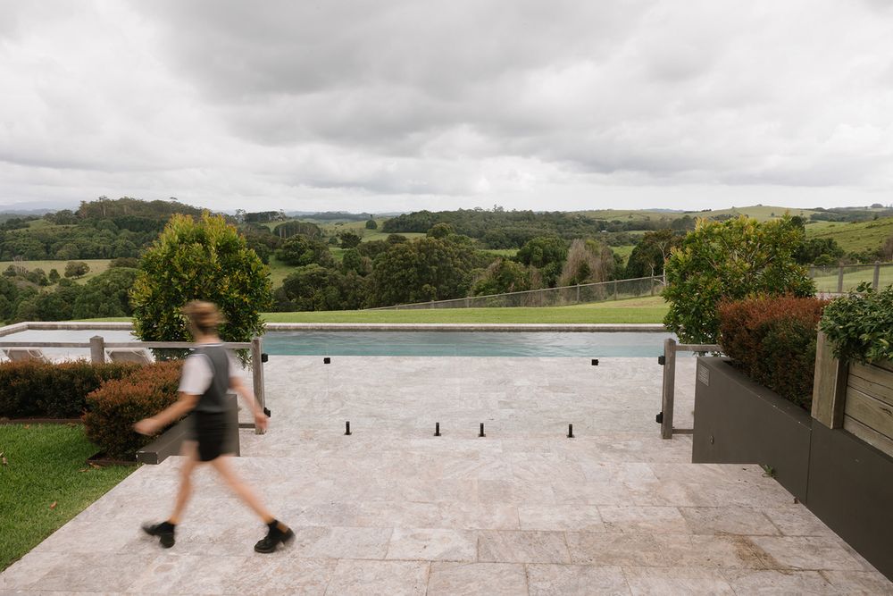Person walking past an infinity pool with panoramic green valley views under cloudy skies at a luxury rural property.