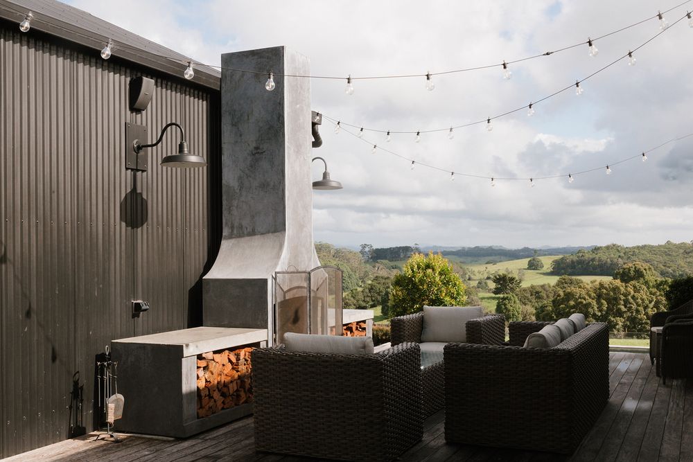 Outdoor deck with wicker furniture, fireplace, string lights, and scenic green hills views.