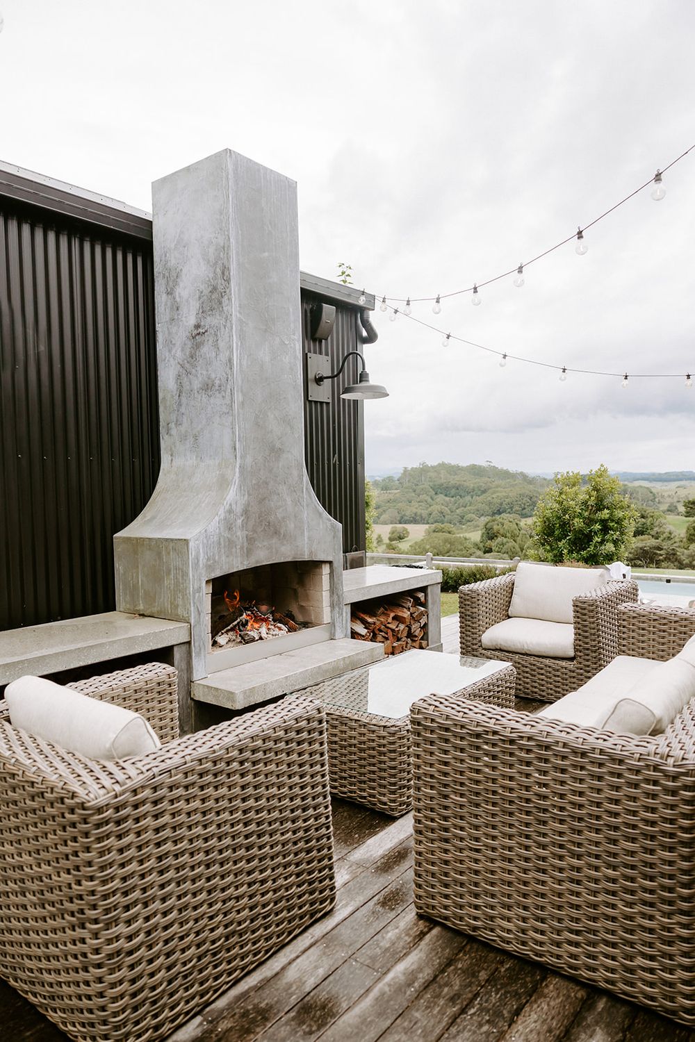 Outdoor patio with wicker furniture, concrete fireplace, string lights, and scenic countryside views.
