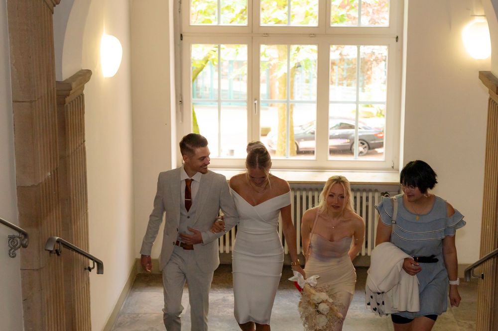 Wedding celebration taking place in a bright indoor venue with arched windows.