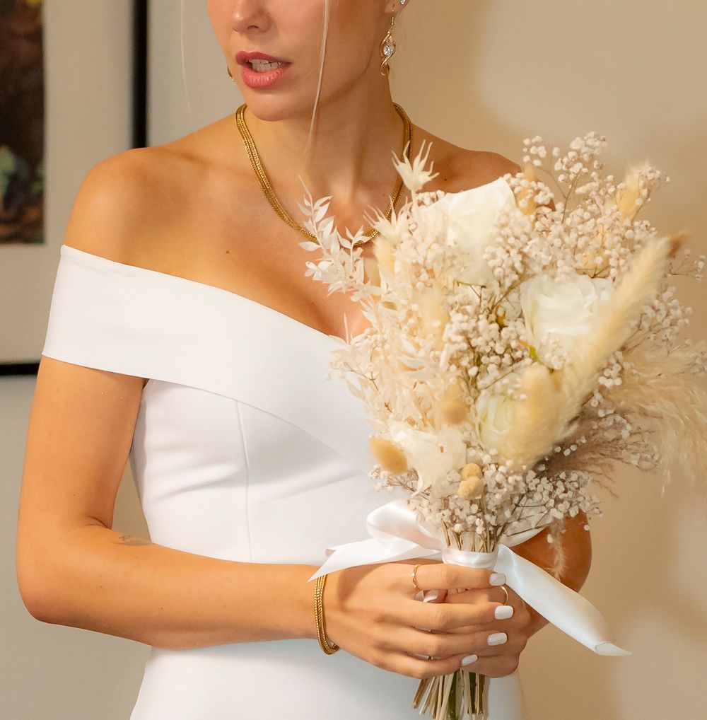 Close-up of white bouquet with dried flowers being held against white dress.