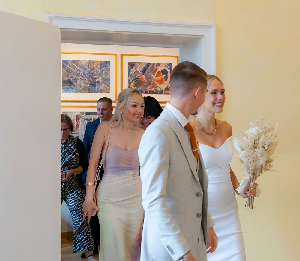 Wedding ceremony guests seated in a bright yellow room with white chairs and decorative floral arrangements.