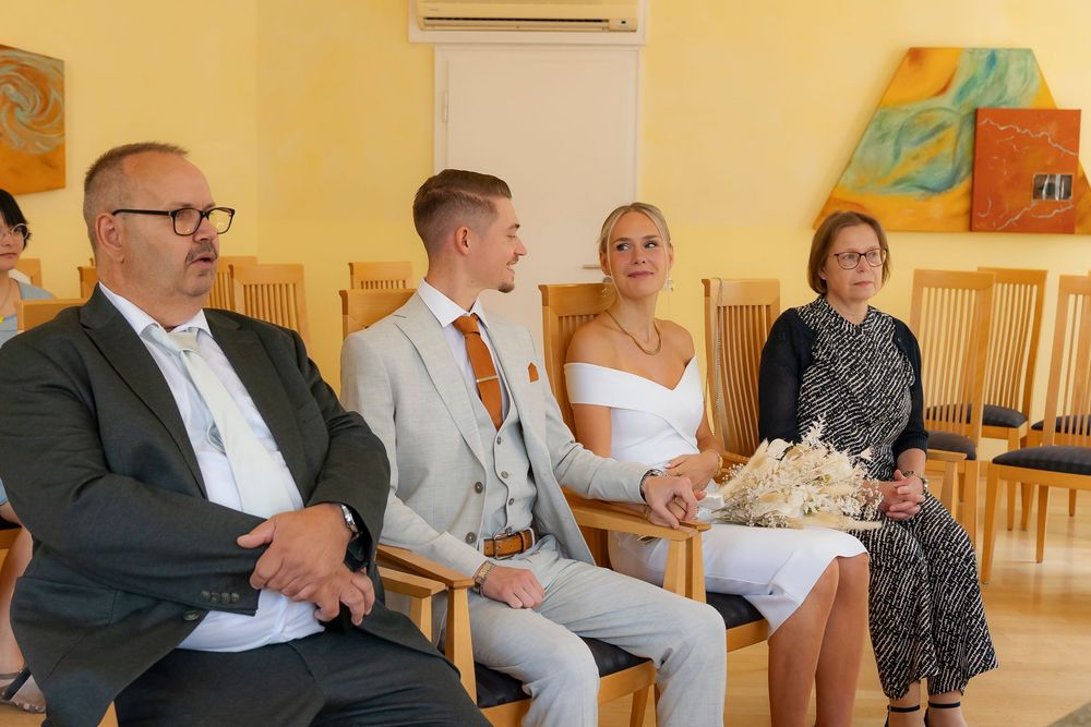 Guests gathered in a yellow-walled room with wooden chairs during a wedding ceremony.