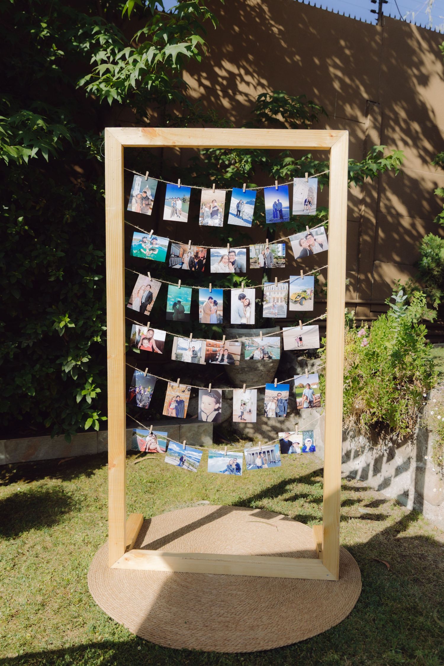 Rustic wooden photo display frame with clothesline strings holding printed photos at an outdoor wedding reception.