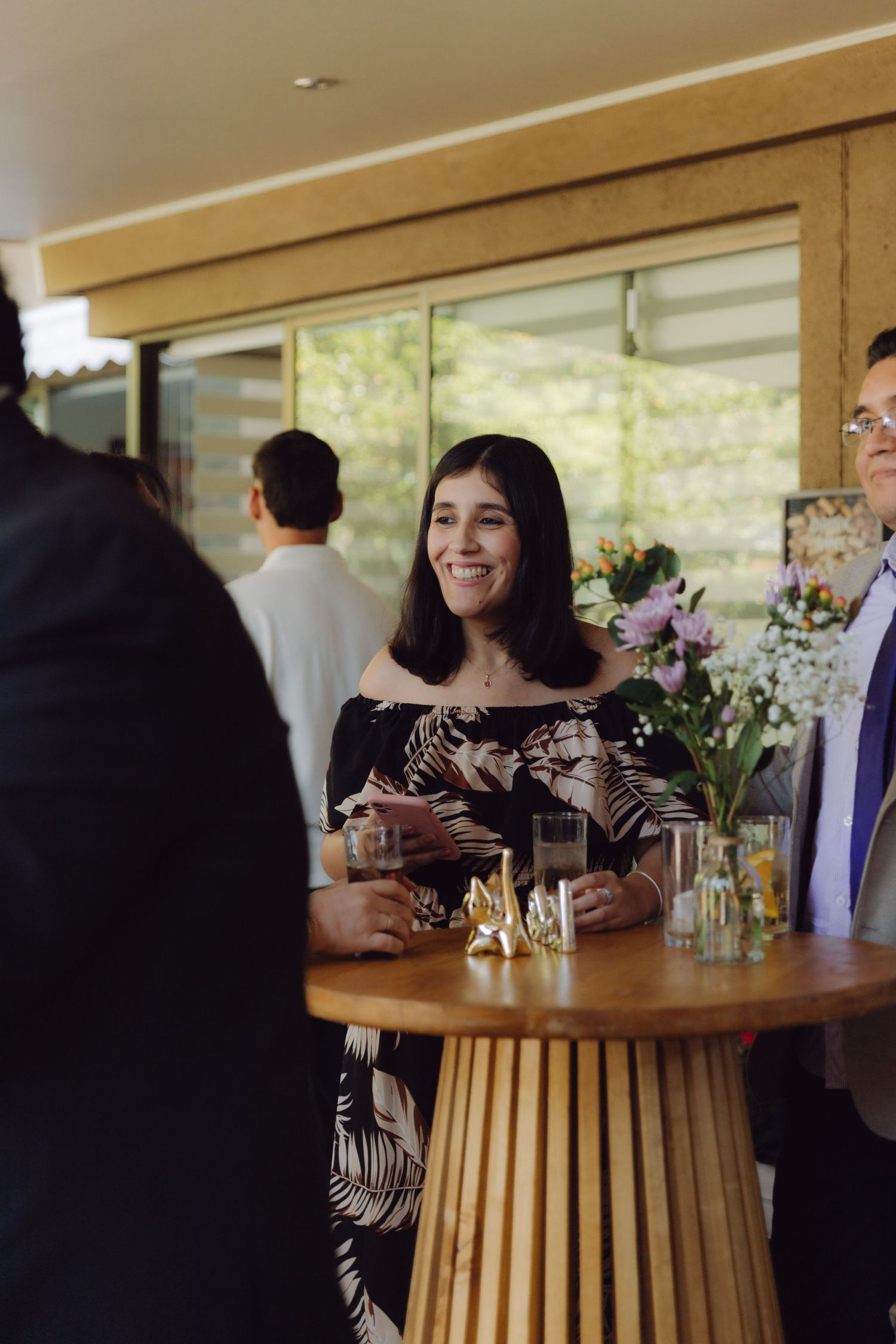 Smiling woman in floral off-shoulder dress socializing at an indoor wedding reception cocktail hour.