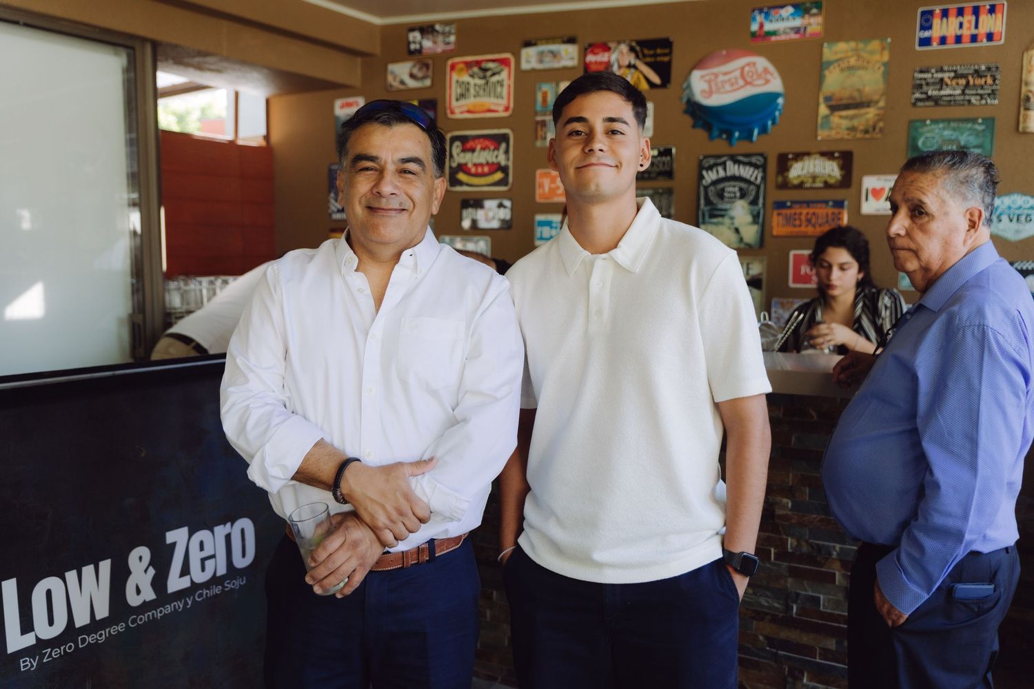 Two men in white shirts posing together inside a restaurant with vintage signs on the wall.