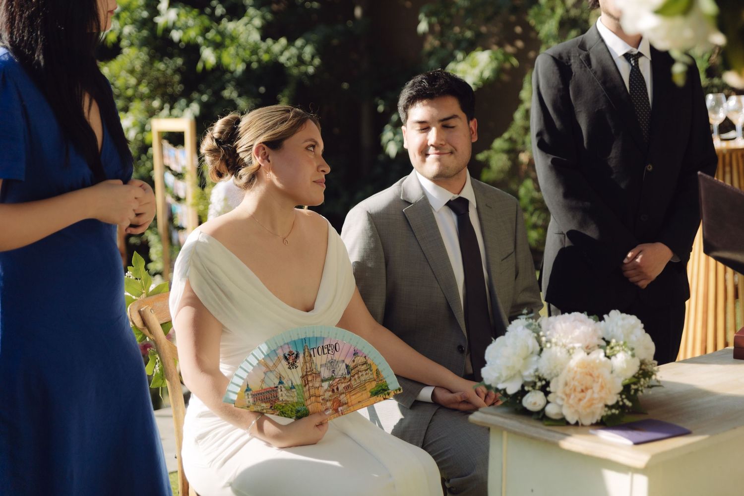 Smiling bride holding decorative fan looks up during romantic outdoor wedding ceremony.