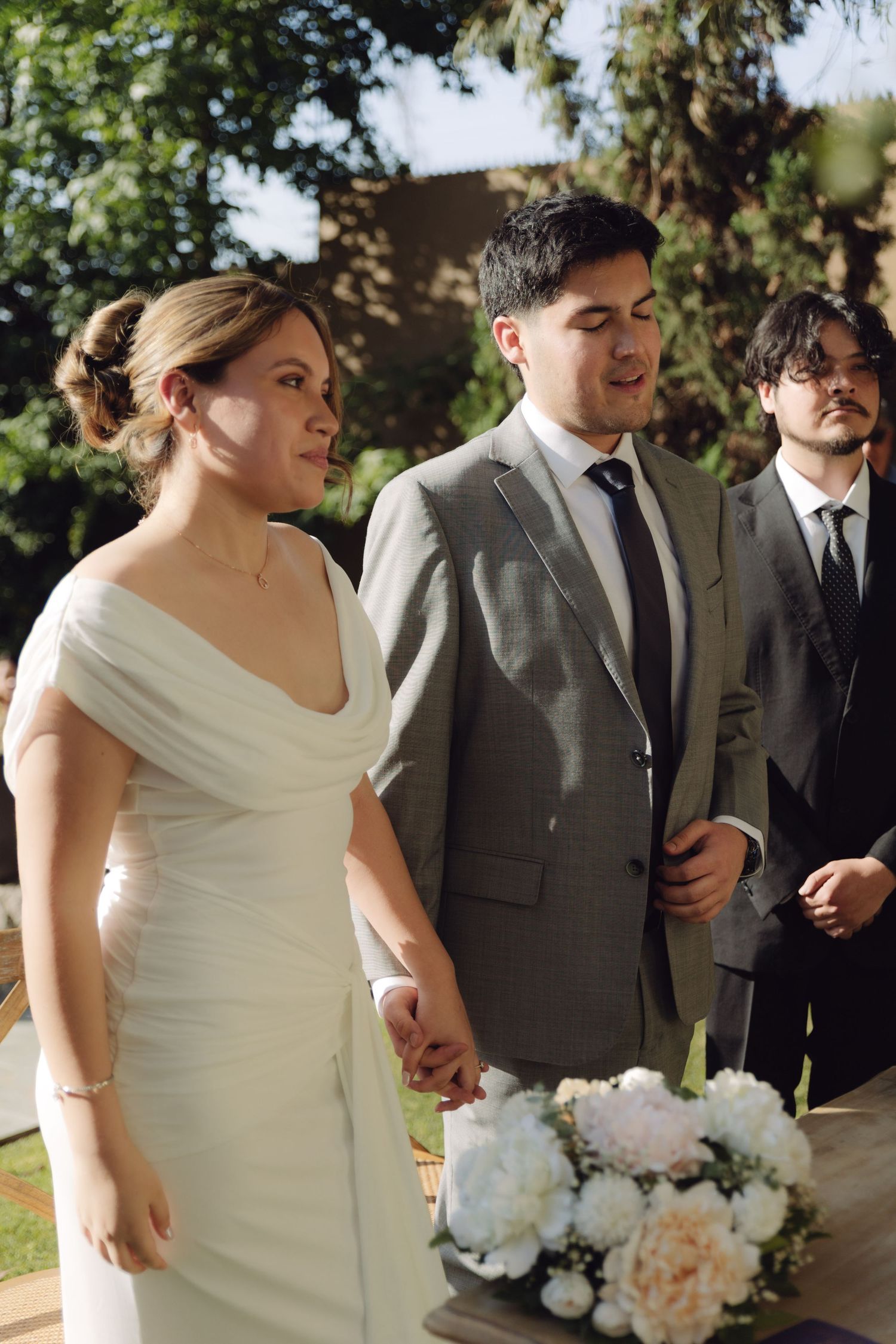 Bride in white gown and groom in gray suit holding hands at outdoor wedding.