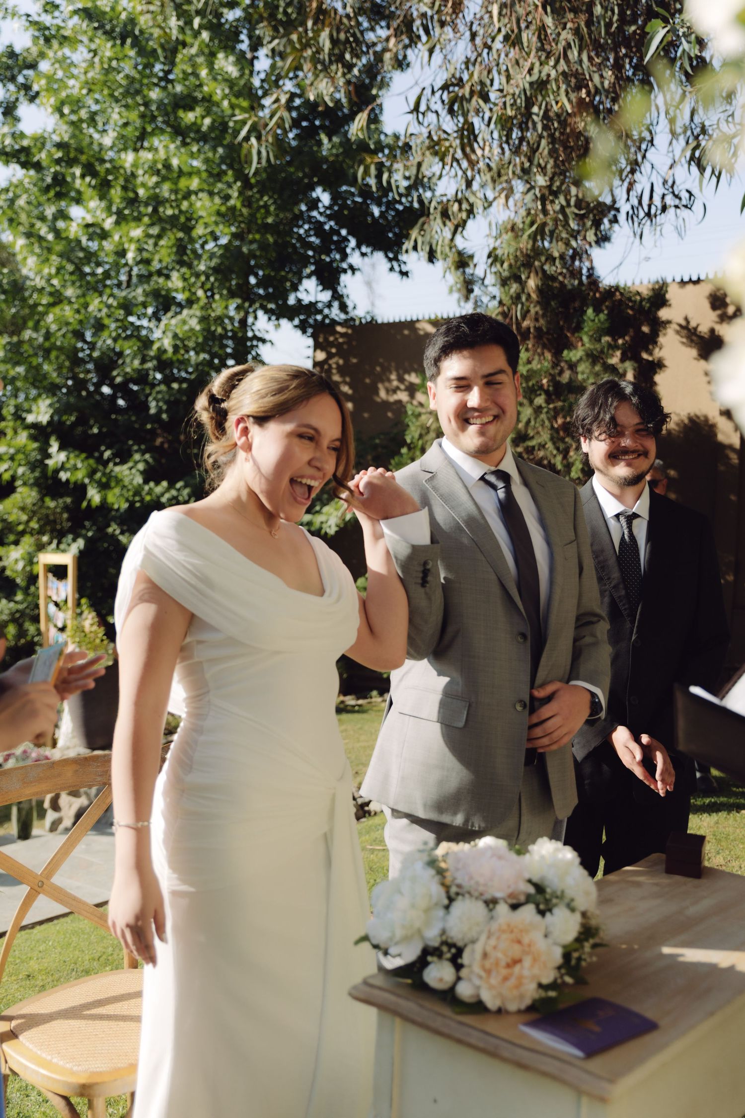 Joyful bride and groom celebrating at outdoor wedding ceremony with white floral bouquet.