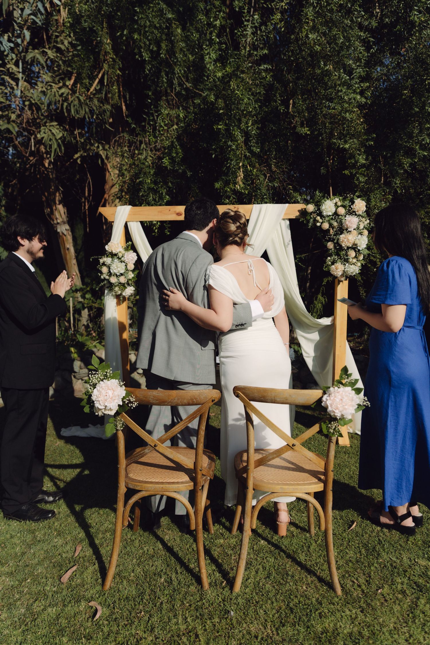 Newlyweds sharing first kiss at decorated outdoor wedding altar with floral arrangements.