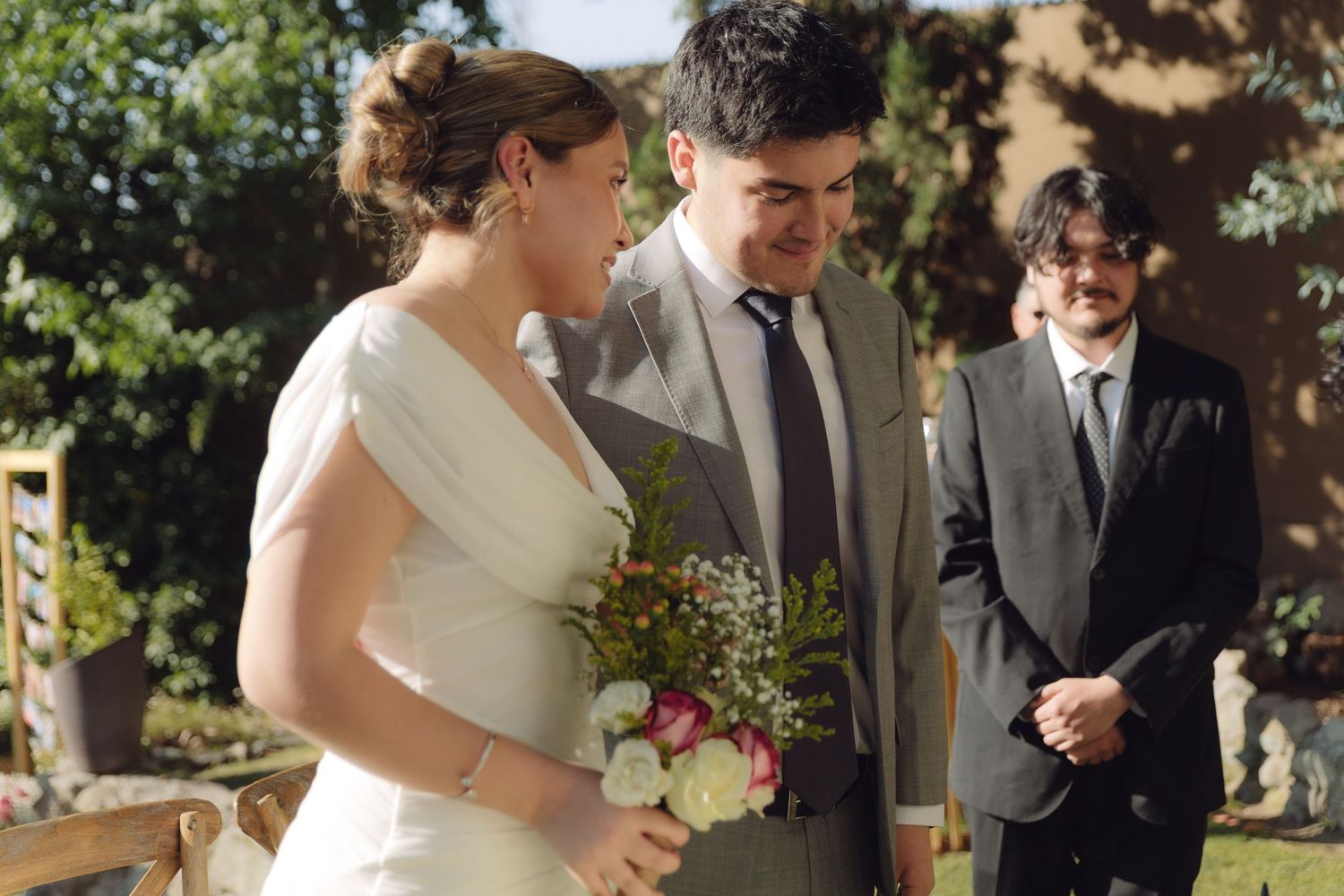 Smiling bride and groom walk together at outdoor wedding ceremony holding a bouquet of flowers.
