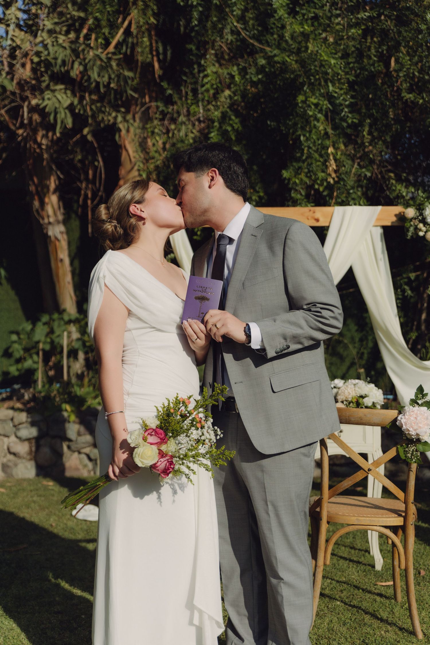 Bride and groom sharing a kiss at outdoor garden wedding ceremony with wooden floral arch behind them.