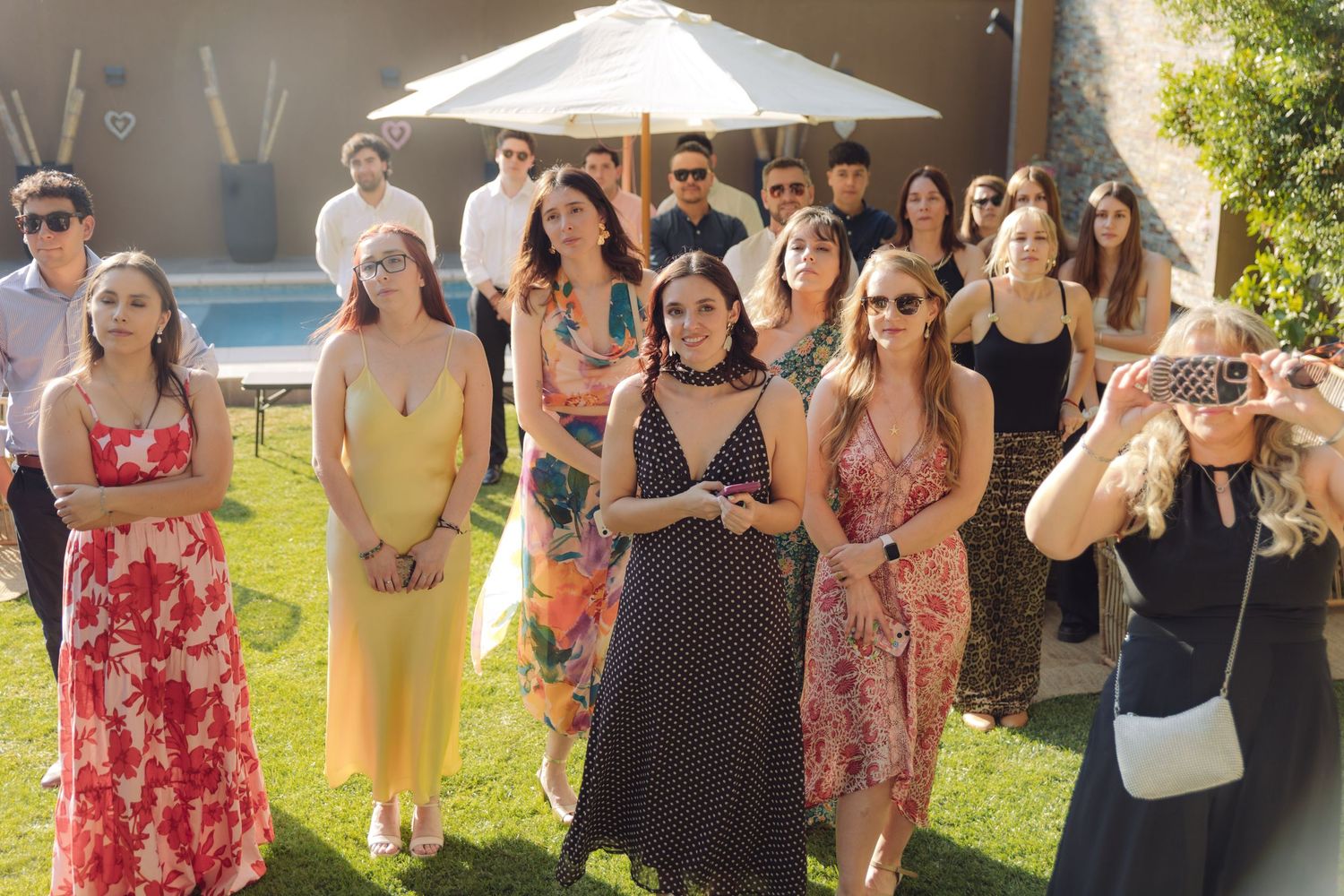 Wedding guests in colorful summer dresses gather outdoors watching the ceremony.