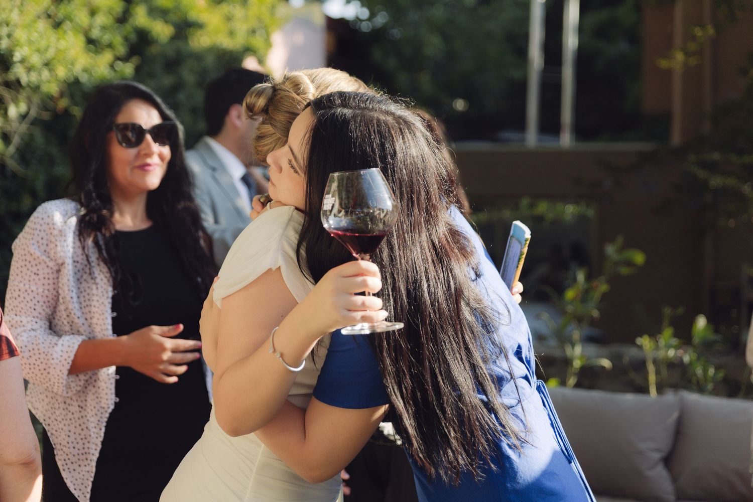 Bride embracing a guest while holding a glass of red wine at wedding reception.