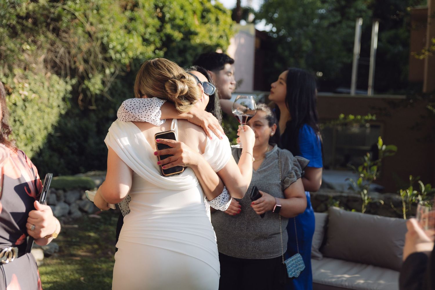 Bride in white dress hugging a guest at an outdoor wedding reception.