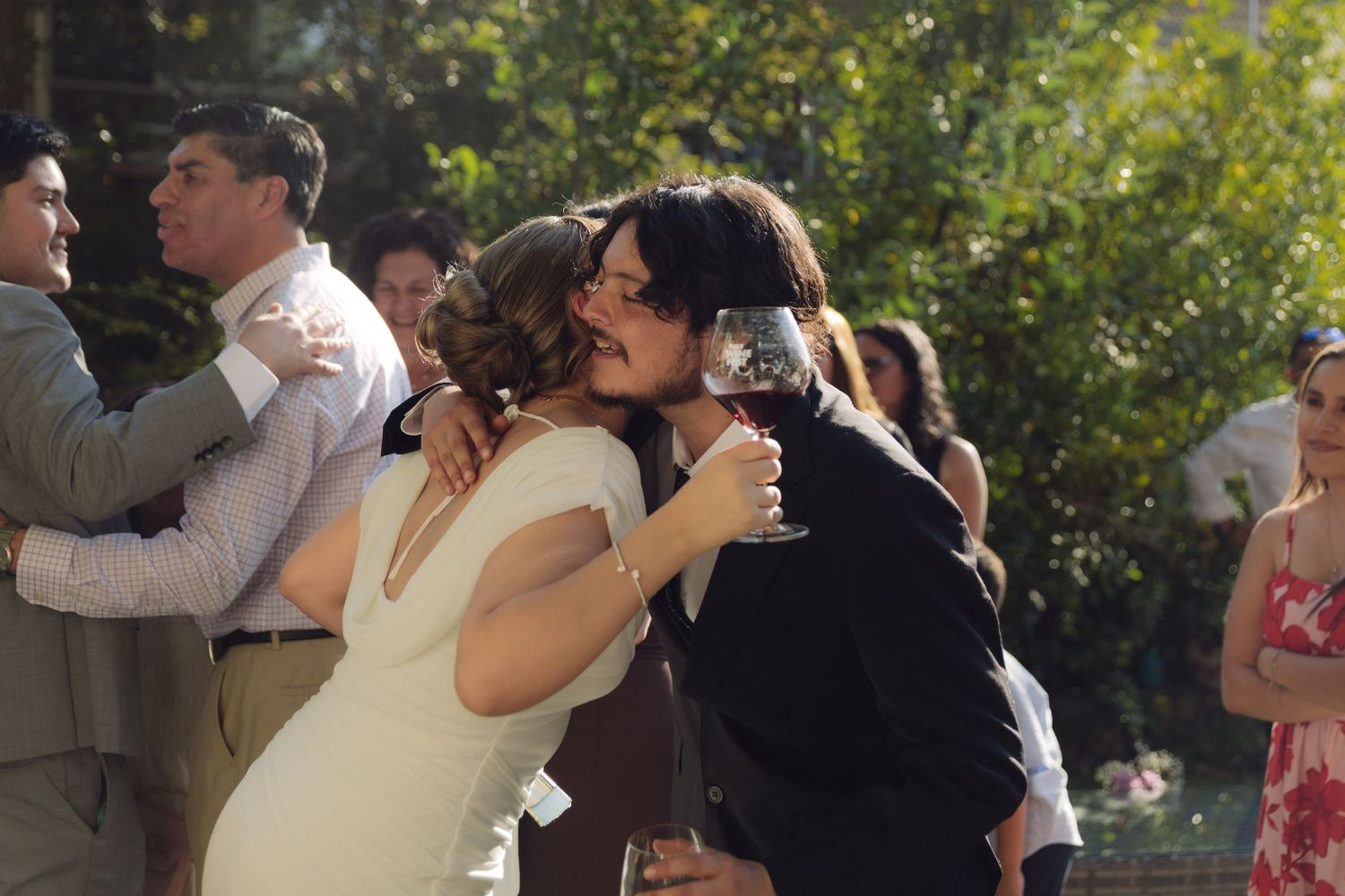 Bride in white dress receiving a kiss on the cheek from a guest at an outdoor wedding.