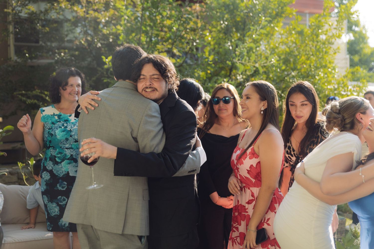 Guests hugging and socializing at a sunny outdoor wedding reception.