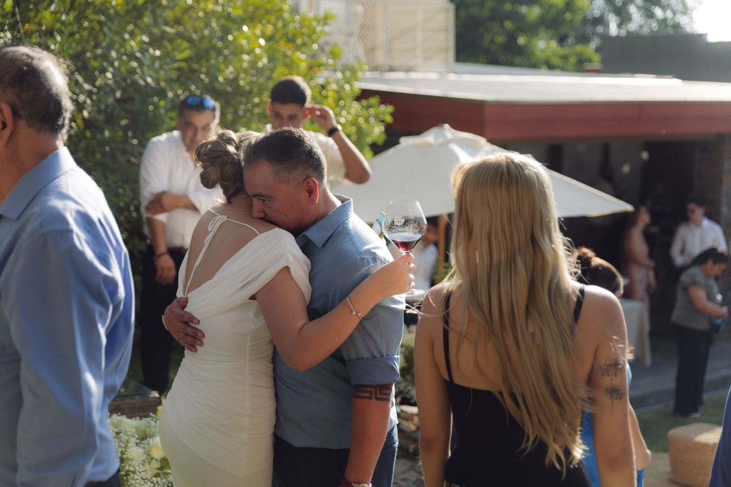 Bride in white dress sharing a warm hug with a male guest at an outdoor wedding.