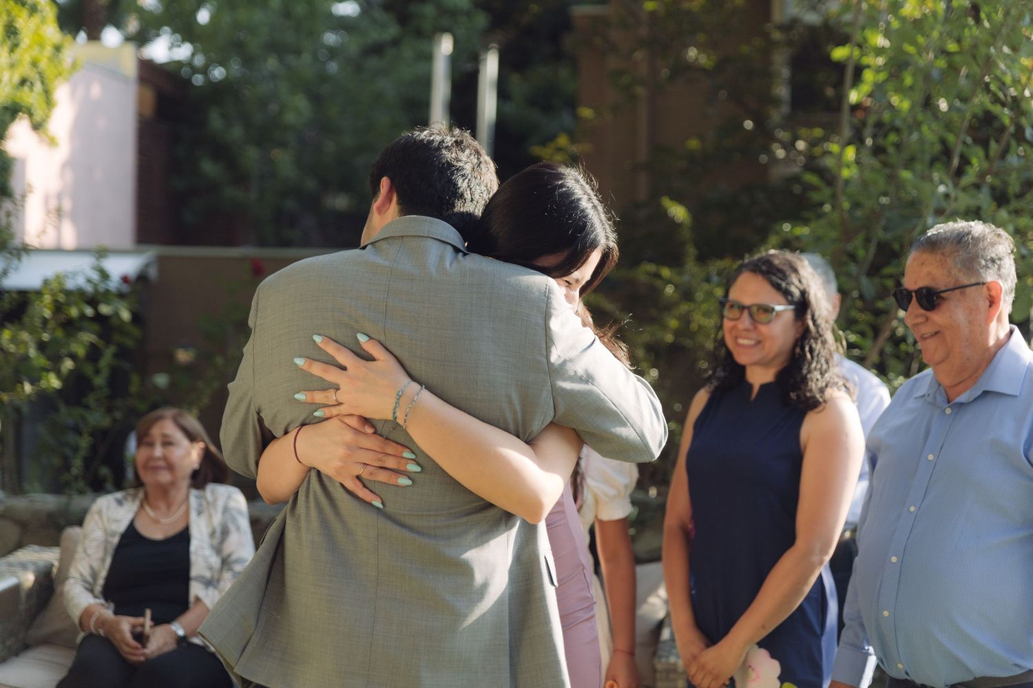 Two guests sharing a heartfelt hug at a sunny outdoor wedding reception.