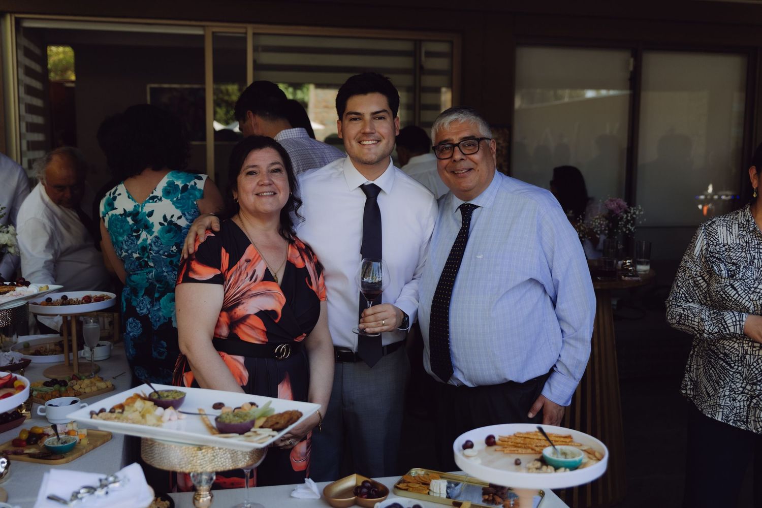 Smiling family trio posing at elegant wedding reception beside table with catered food.