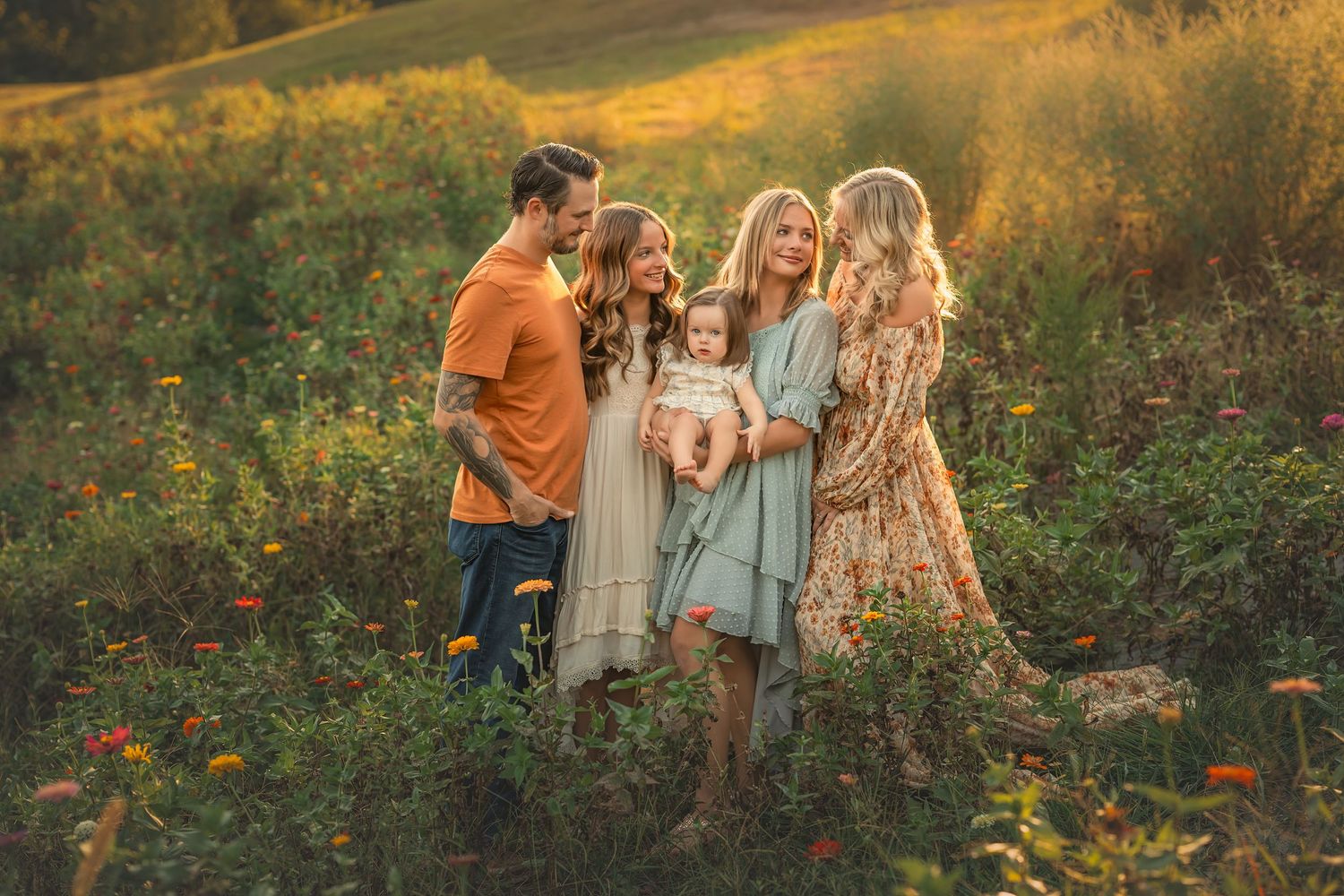 Couple embracing romantically in a vibrant wildflower field at golden hour, wearing floral dress and orange shirt.