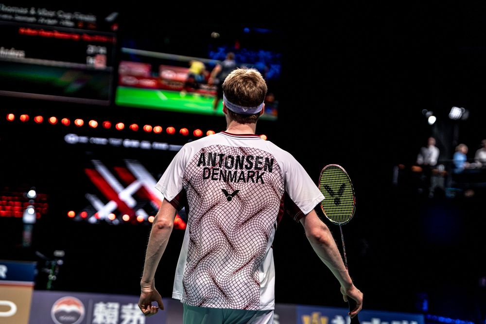 Antonsen Denmark badminton player seen from behind holding racket on court during competitive match.