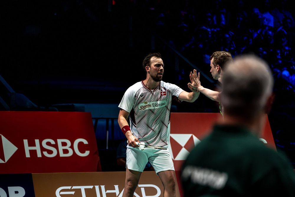 Two badminton players in green uniforms celebrate with a high-five during a competitive match at an HSBC tournament.