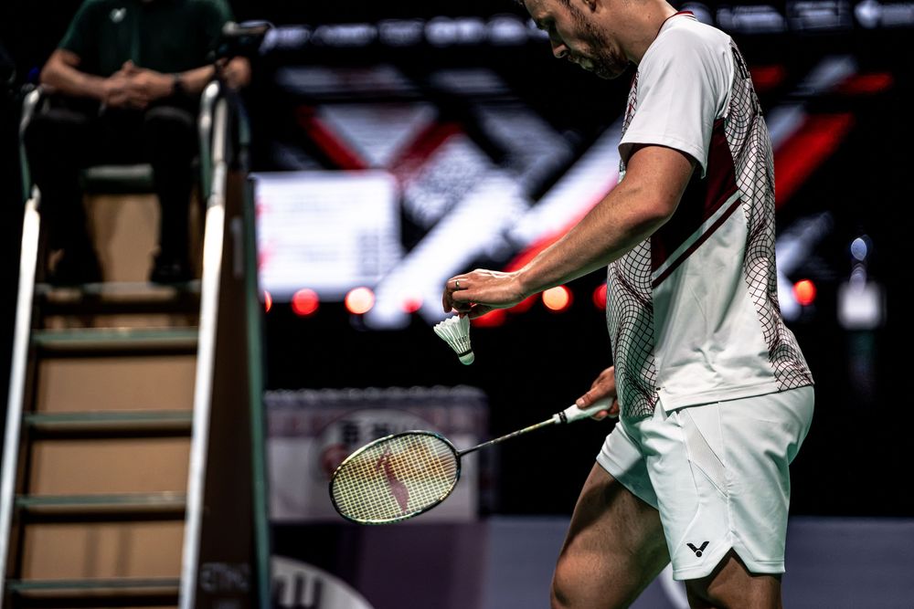 Badminton player holding a racket and shuttlecock courtside during a professional indoor tournament match.