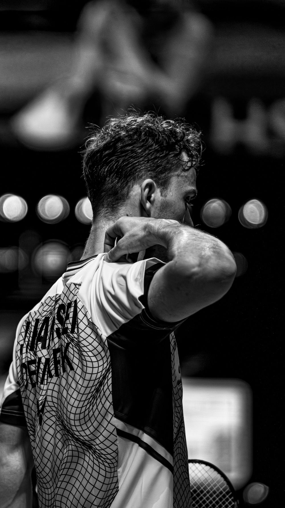 Black and white photo of a tennis player wiping his face with his arm during an intense match.