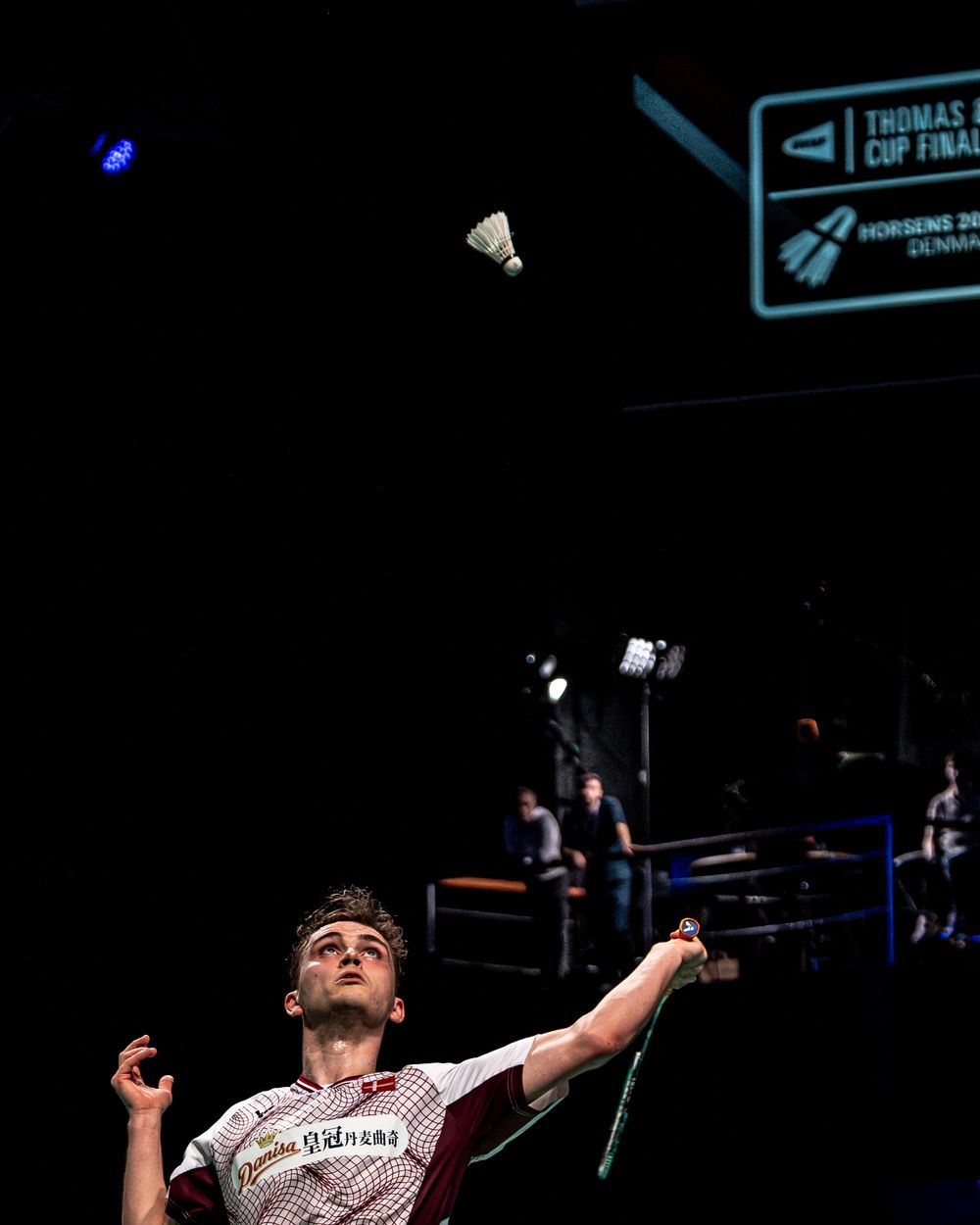 Badminton player reaches up to serve shuttlecock at Thomas Cup Finals in Horsens, Denmark.