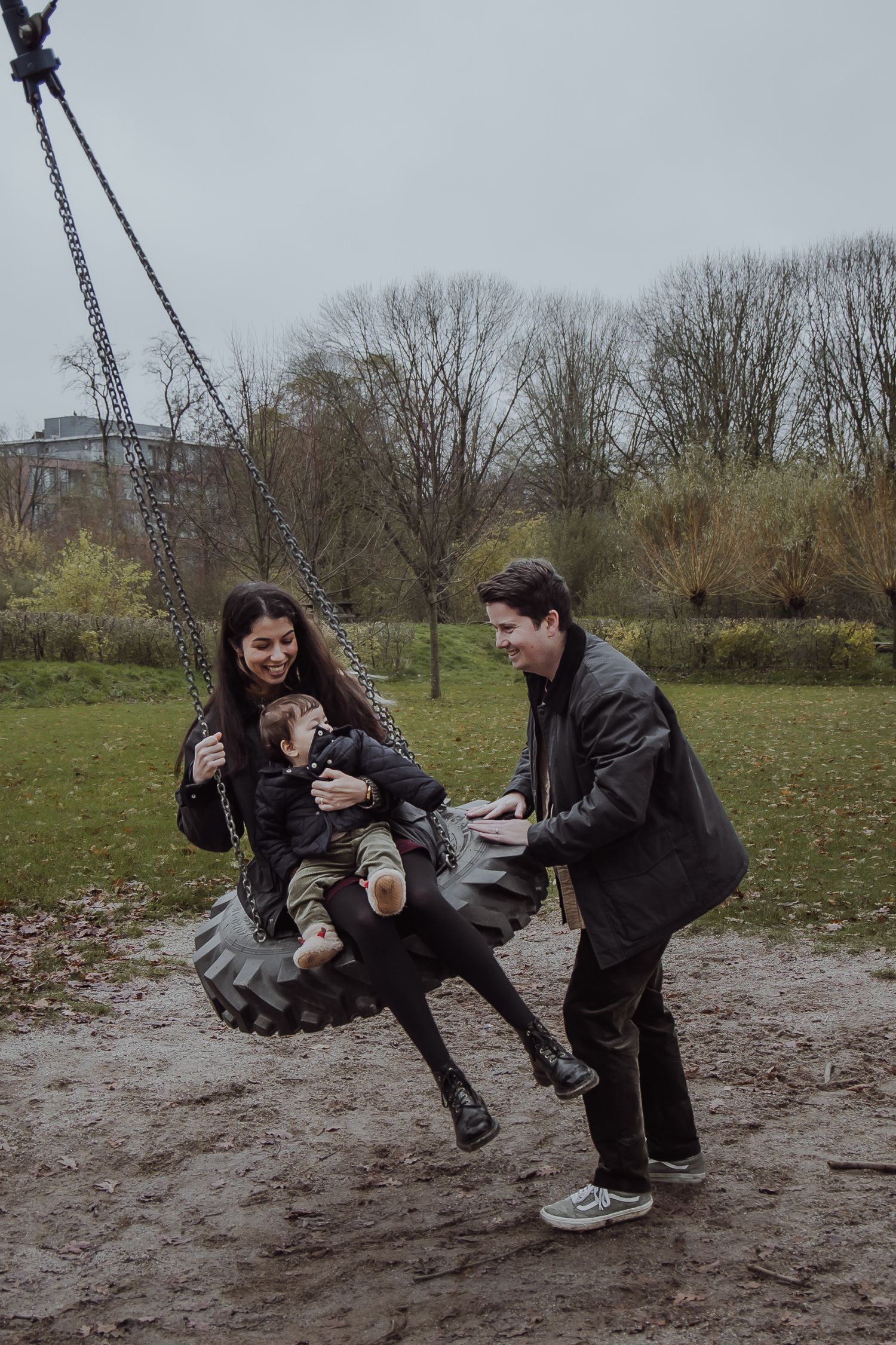 Dad pushing mum and their baby on a swing during a winter family photoshoot in a park in Woerden
