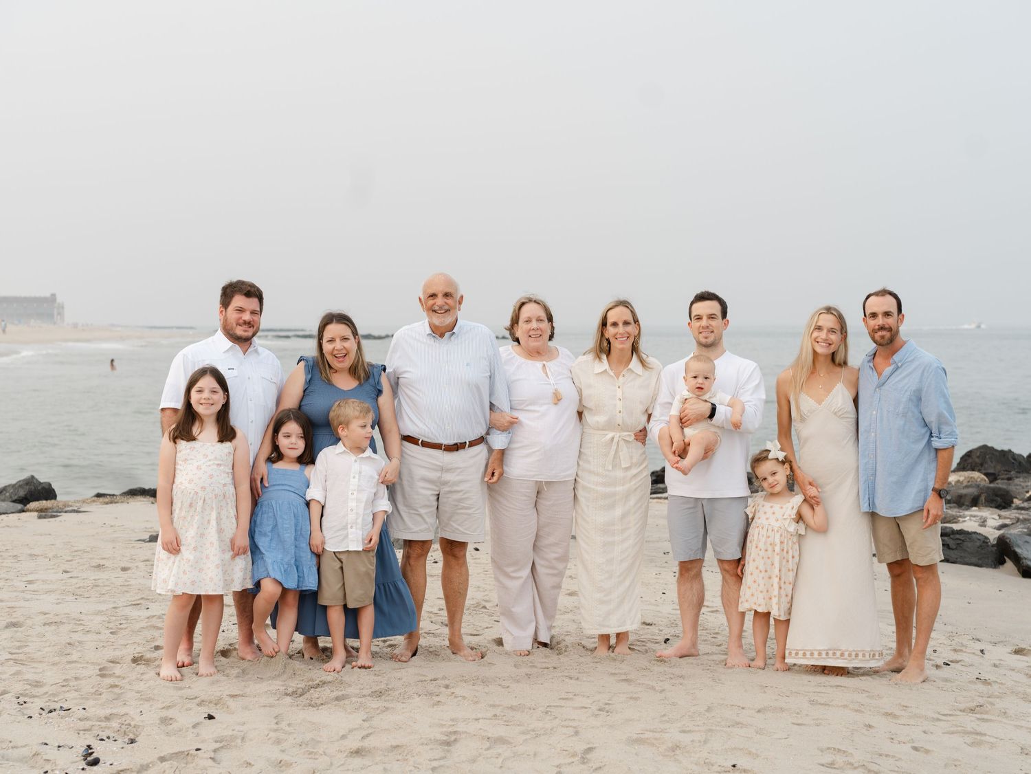 Large extended family smiling together on the oceanfront beach in Ocean Grove NJ at sunset.