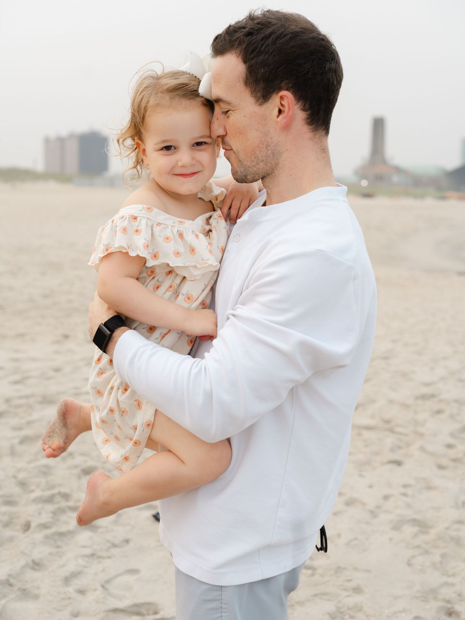 Father in a white shirt holds his daughter on the sand in Ocean Grove.