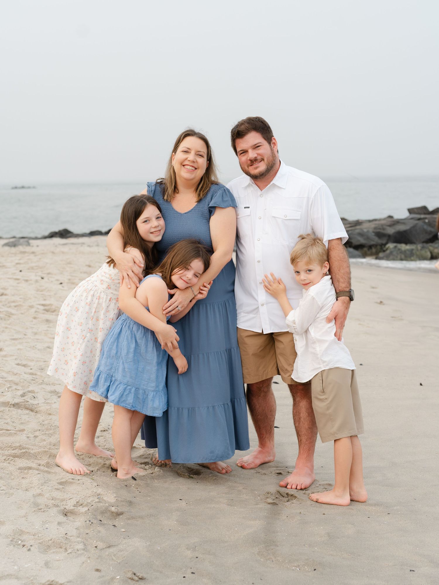 Family of 5 barefoot family members standing together in the ocean surf at golden hour.