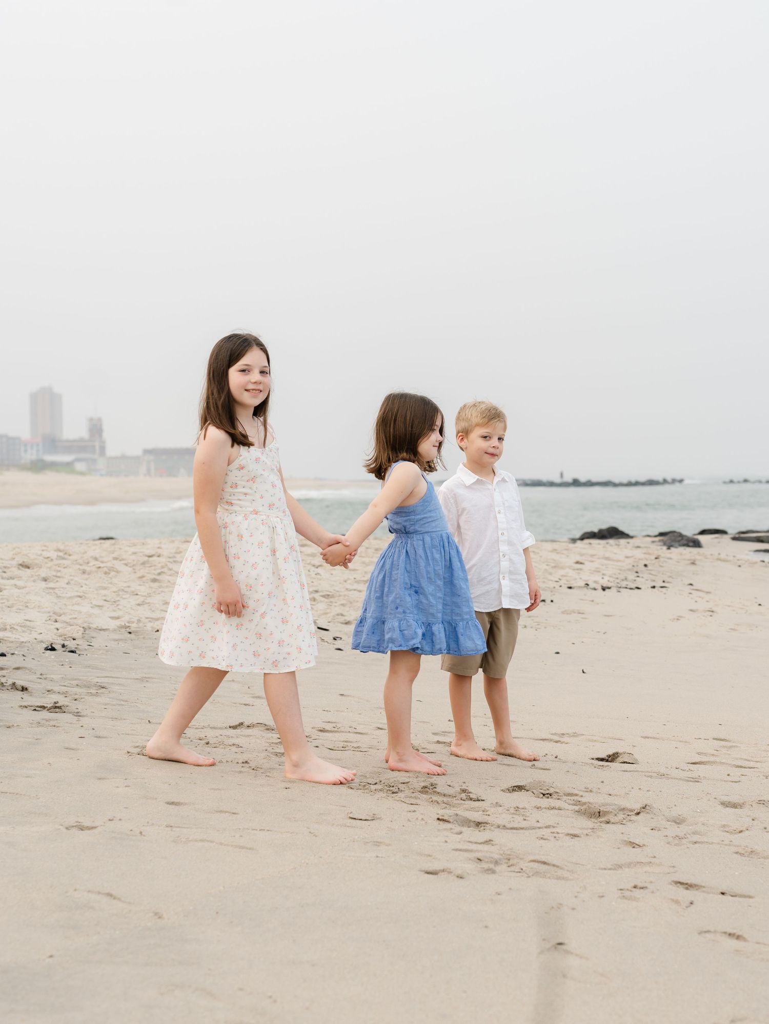 Siblings hold hands looking out at the ocean while lauren marie photography captures the beautiful moment.