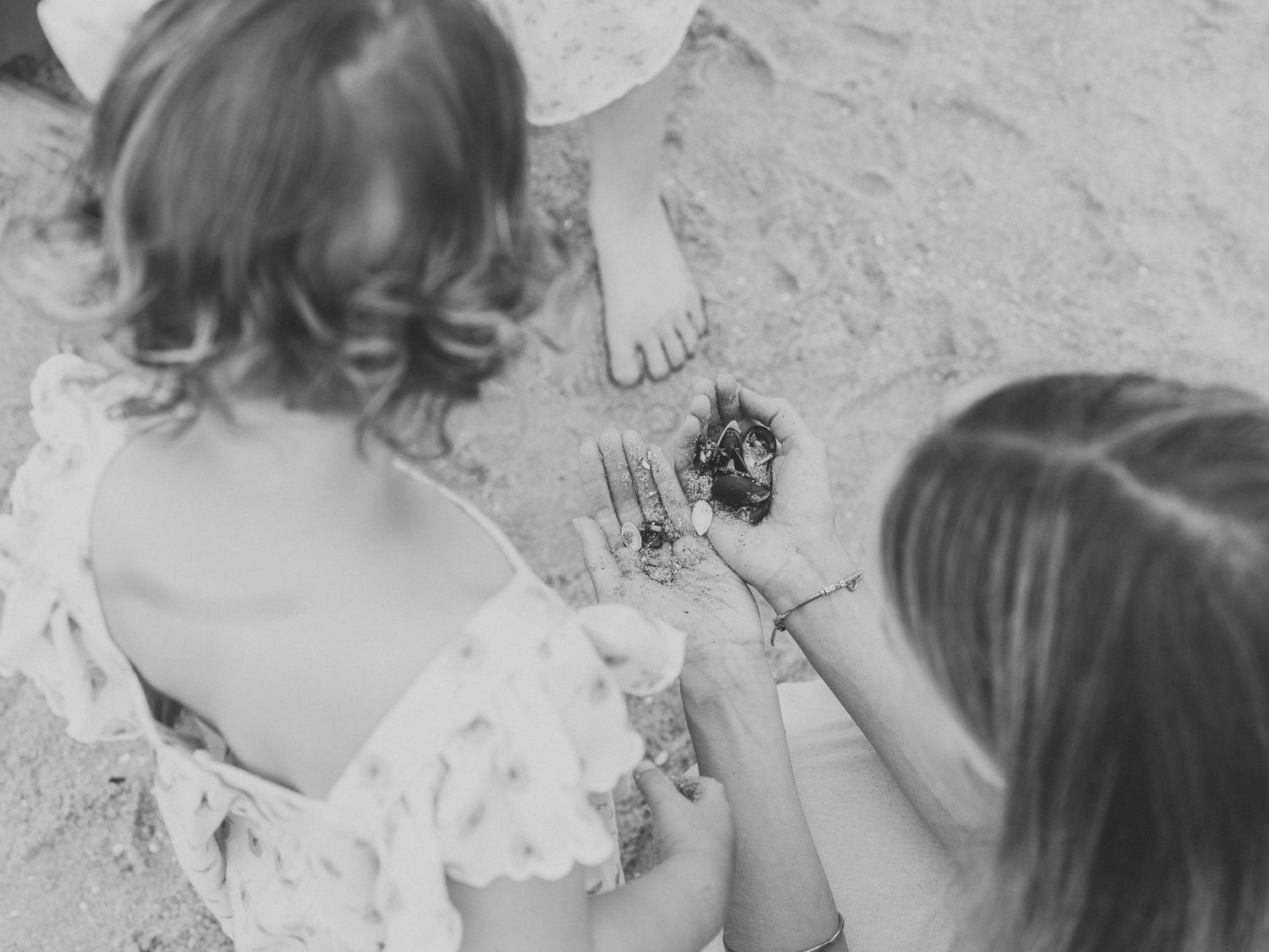 Close up of an aunt and her nieces on the beach playing with shells.