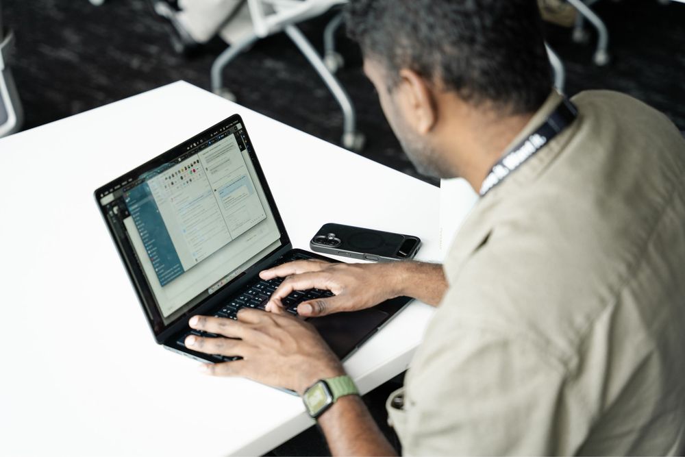 Man working on laptop at white desk with smartphone nearby, focused on screen displaying data charts.