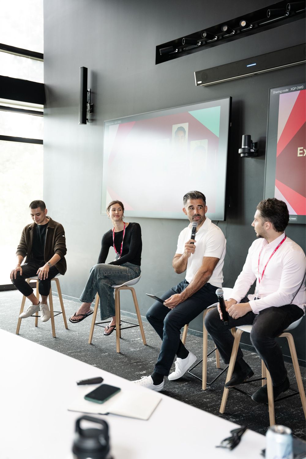 Four professionals engaged in a panel discussion seated on stools in a modern conference room with a presentation screen.