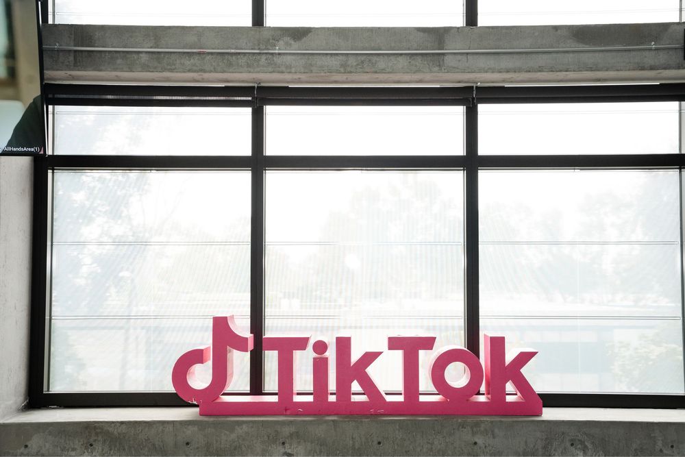 Pink TikTok logo sign displayed on a concrete wall in front of large windows at TikTok headquarters.