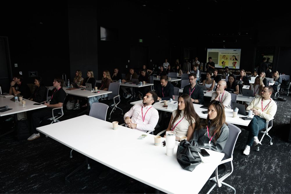Audience of professionals attending a conference presentation in a modern dark-walled event venue with white tables.