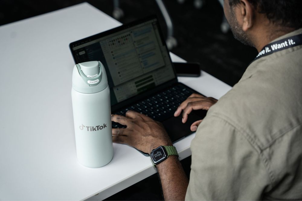 Person typing on laptop next to a TikTok branded white water bottle on a white desk.