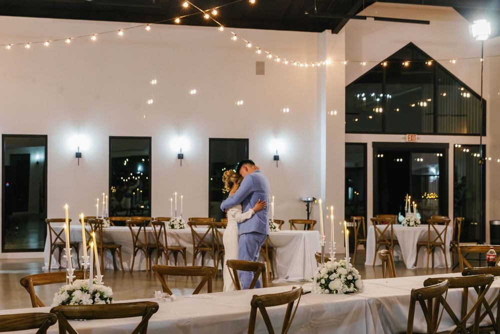 Bride and groom embracing during a private first dance inside a modern wedding reception venue illuminated by string lights.