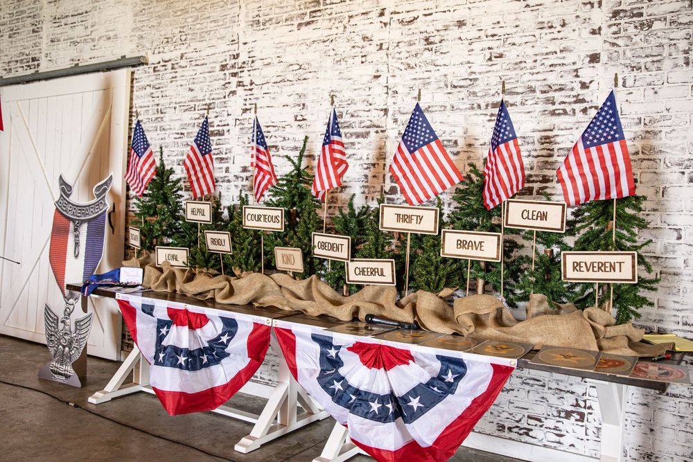 Patriotic holiday display with American flags, greenery, and red white blue bunting on a rustic wooden table against brick wall.