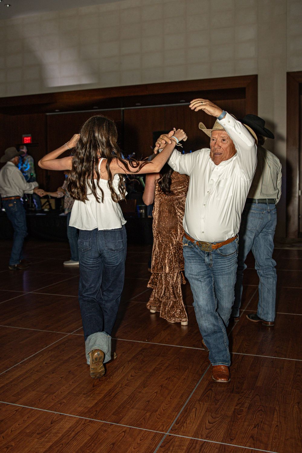 Couple line dancing in cowboy hats at a country western event on a hardwood dance floor.