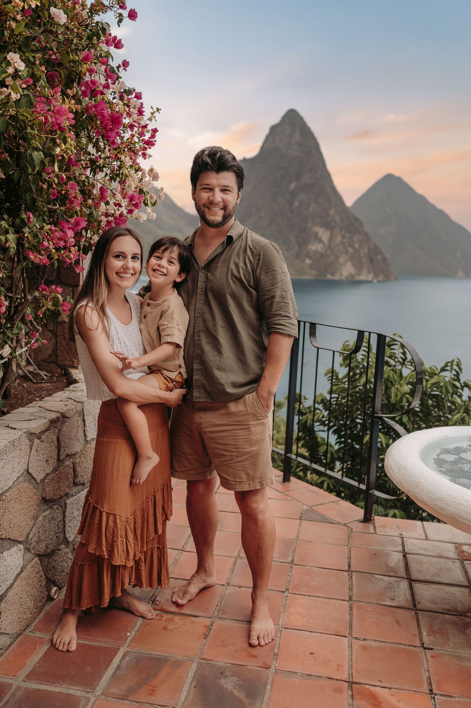 Family of three with a little boy stands in front of beautiful ocean backdrop, smiling at camera