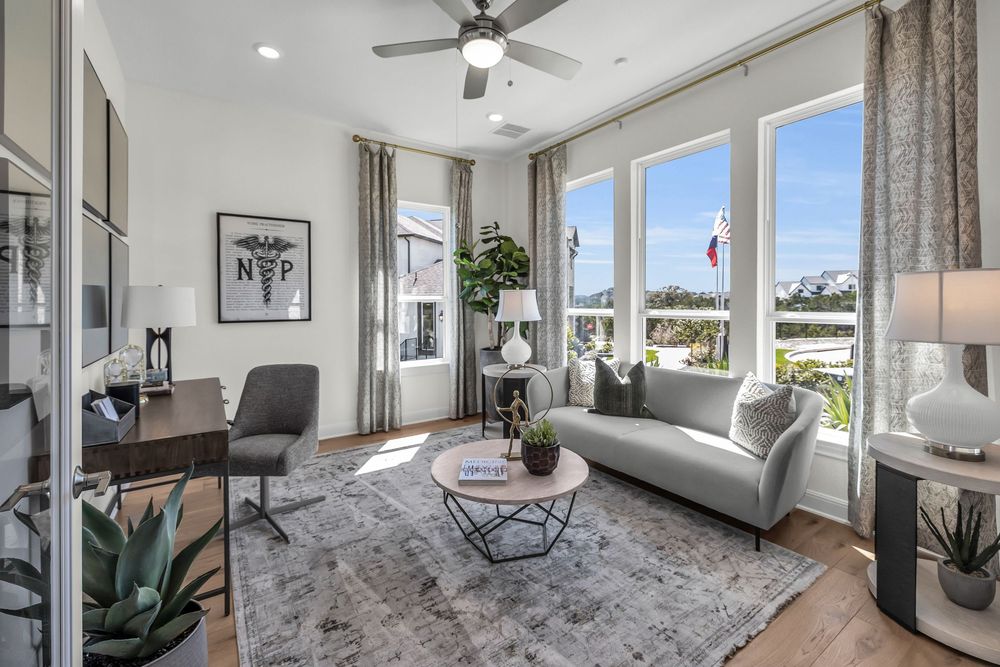 Bright modern living room with gray sofa, ceiling fan, large windows, hardwood floors, and stylish decor.