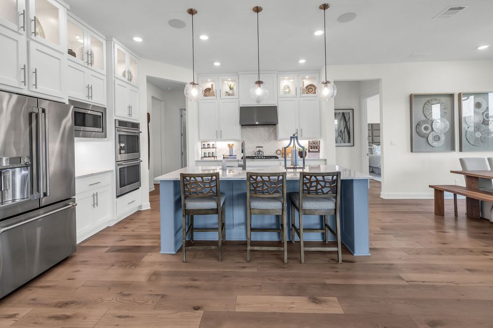 Modern kitchen with blue island, white cabinets, hardwood floors, and stainless steel appliances under pendant lights.