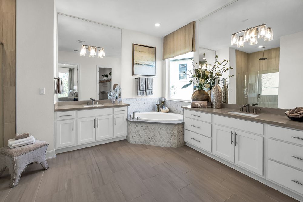 Spacious master bathroom with white cabinets, dual vanities, corner soaking tub, and wood-look flooring.
