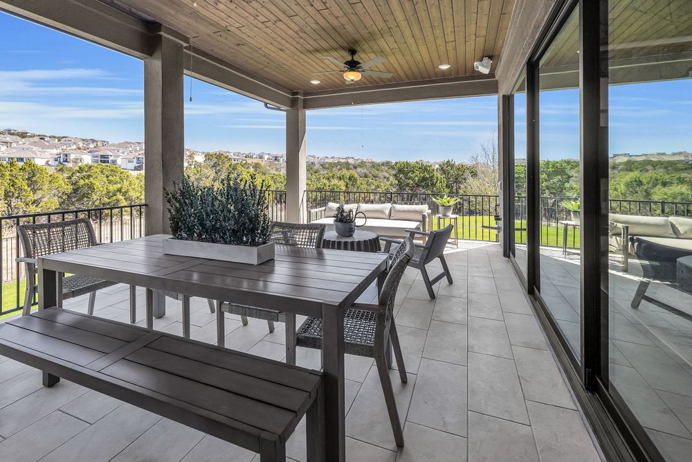 Covered outdoor patio with dining table, bench seating, ceiling fan, and panoramic views of rolling hills and neighborhood.