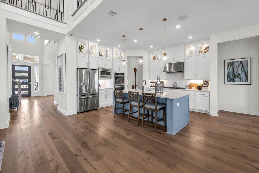 Modern open-concept kitchen with blue island, white cabinets, stainless steel appliances, and dark hardwood floors.